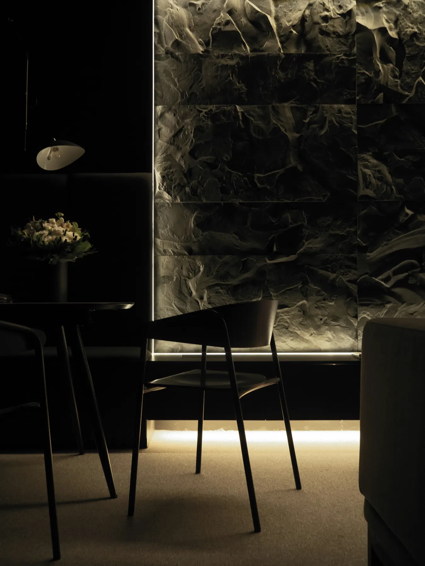 A dark private room: two chairs at a small table, a stone wall lit from below