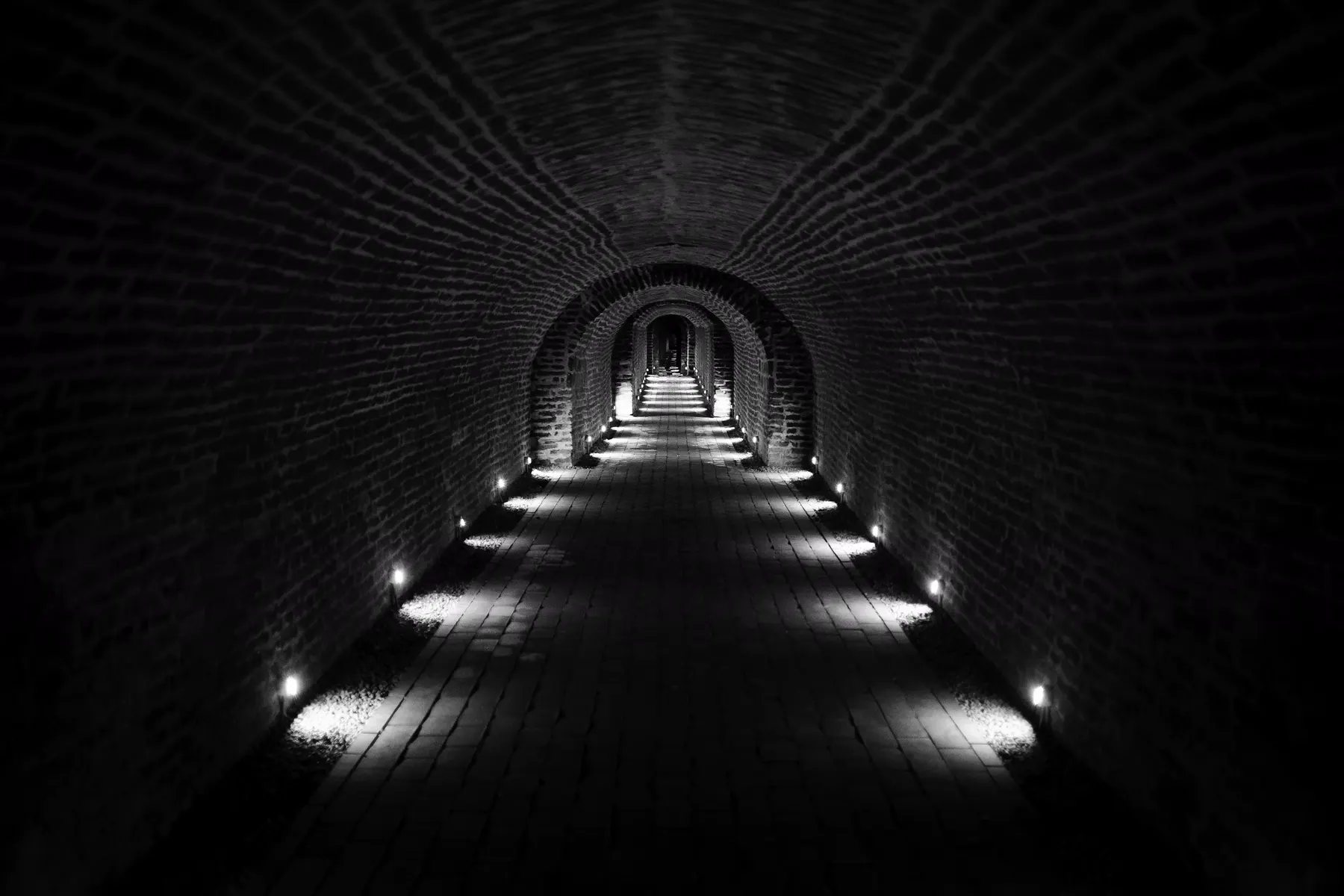 A long vaulted brick corridor, lit by small lamps set low along the floor